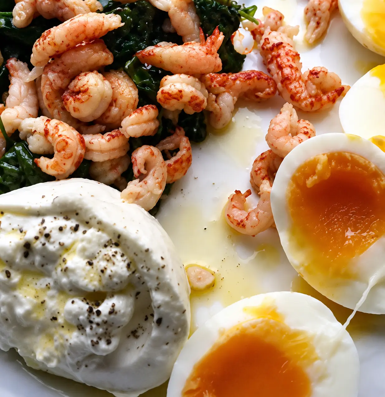 Almuerzo keto con gambas salteadas, espinacas, huevos pasados por agua y burrata cremosa.